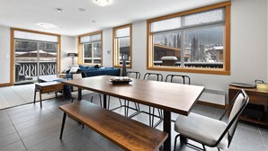 Et moderne spiseområde med et stort træbord, bænke og stole. Store vinduer med satin glas og udsigt til et sneklædt landskab.