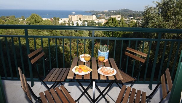 A balcony with a table set for two, featuring a meal and drinks, overlooking a coastal cityscape. - Blue & Green Apts - Dassia, Corfu 4 (Corfu)