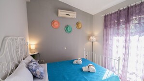 A bedroom with a blue bedspread, white headboard, and a wall-mounted air conditioner. - Blue & Green Apts - Dassia, Corfu 4 (Corfu)