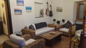 A cozy living room with wicker furniture, a white sofa, and a coffee table. There are paintings on the wall and a guitar hanging above the sofa. - A cute, homey cottage overlooking the Apuan Alps . A perfect place to relax in. (Casone Carpinelli)