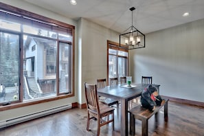 A dining area with a large table, chairs, and a hanging light fixture.