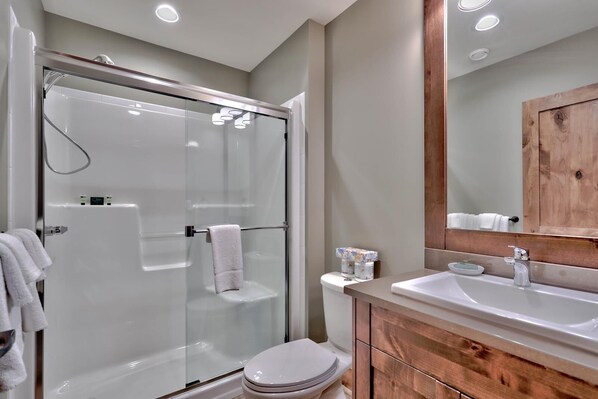 A modern bathroom with a glass-enclosed shower, a wooden vanity with a sink, and a toilet.