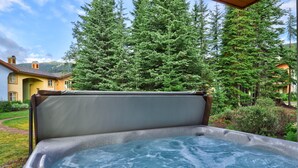 A hot tub in a garden with a view of a house and tall trees. - Ground floor 2 bedroom condo with easy access to ski runs (Sun Peaks)