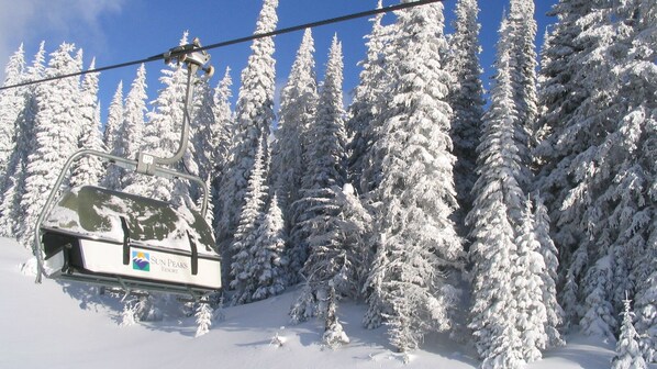Un télésiège avec l’inscription « Sun Peaks Resort », entouré d’arbres couverts de neige.