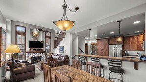 A spacious living area with a fireplace, a dining table, and a kitchen with wooden cabinets and a stainless steel refrigerator. - Spacious multi level 3 bedroom + den townhouse, close to Morrisey lift (Sun Peaks)