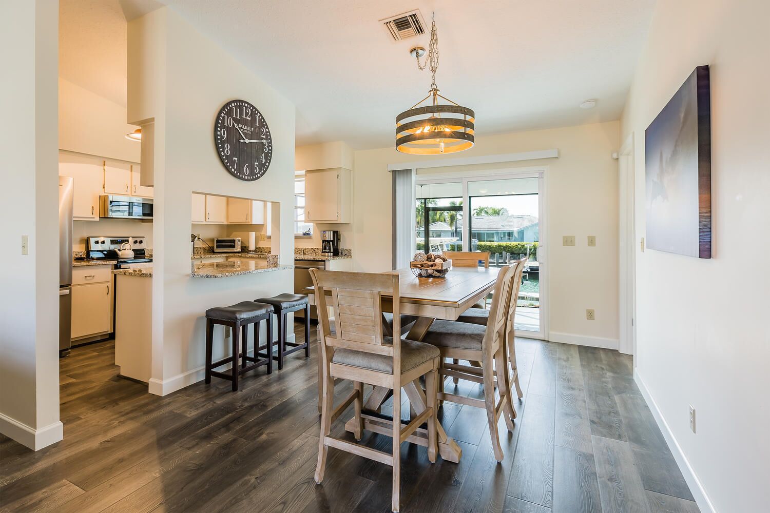 A modern kitchen with a dining area, wooden flooring, and a large clock on the wall.