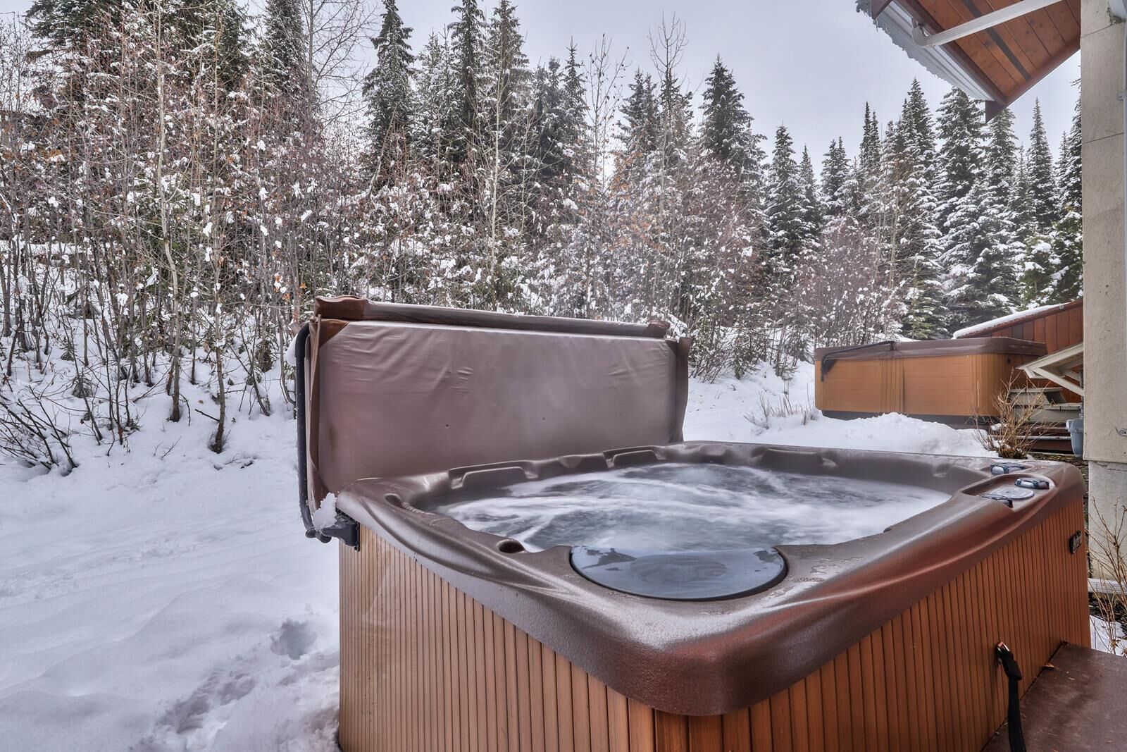 Ein Whirlpool im Freien mit Holzverkleidung, umgeben von schneebedeckten Bäumen und einer Holzterrasse.