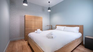 Una cama bien hecha con sábanas y toallas blancas, un armario de madera y dos lámparas colgantes.