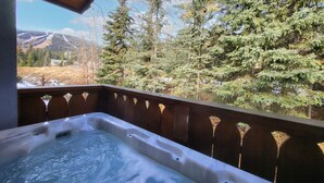 A hot tub on a wooden deck with a view of a forest and mountains. - Cozy Condo Close to Village | Access to Ski-Out Trail | Private Hot Tub | Fireplace (Sun Peaks)