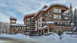 A multi-story hotel with a ski lodge, balconies, and a stone tower. - Modern 1 bedroom apartment in village centre (Sun Peaks)