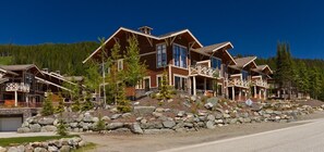 Cabins feature rustic architectural style with prominent beams and large windows, set amidst a well-maintained garden.
