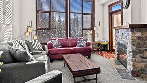 Ein Wohnzimmer mit einem roten Sofa, einem grauen Sofa, einem Holztisch und einem Kamin aus Stein.
