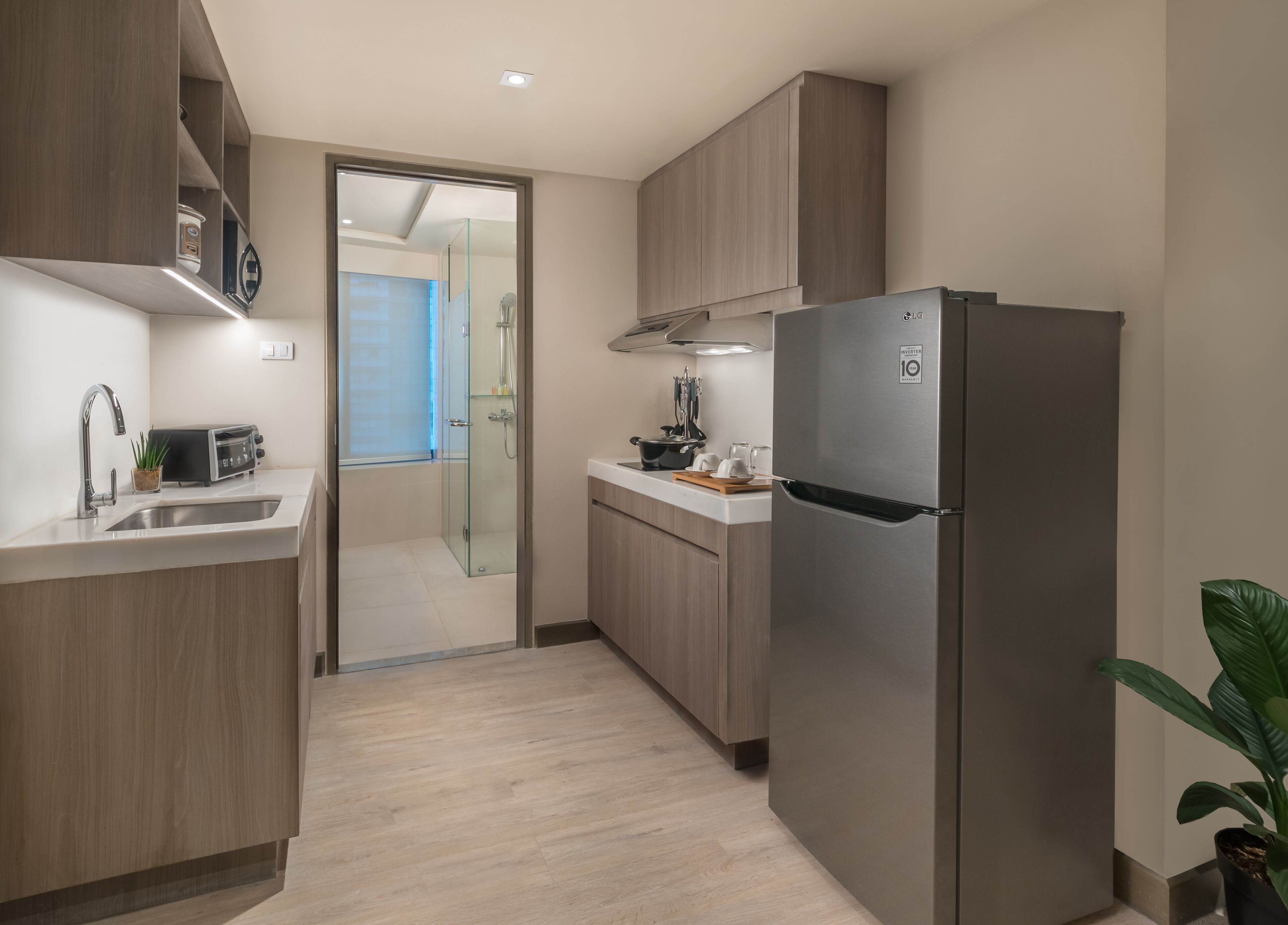 A modern kitchen with wooden cabinets, a stainless steel refrigerator, a built-in oven, and a glass shower enclosure.
