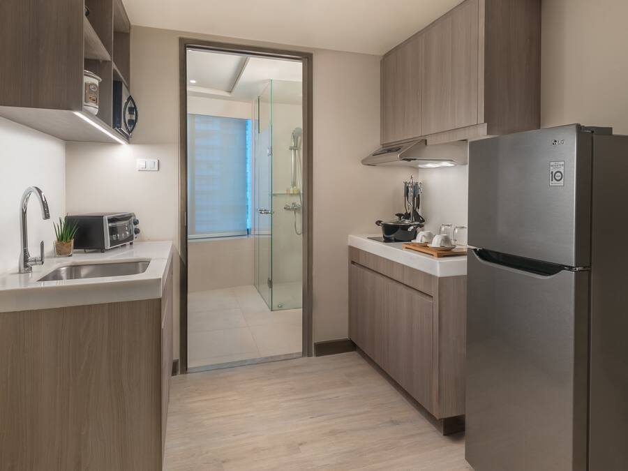 A modern kitchen with wooden cabinets, a stainless steel refrigerator, a toaster, and a glass shower enclosure.