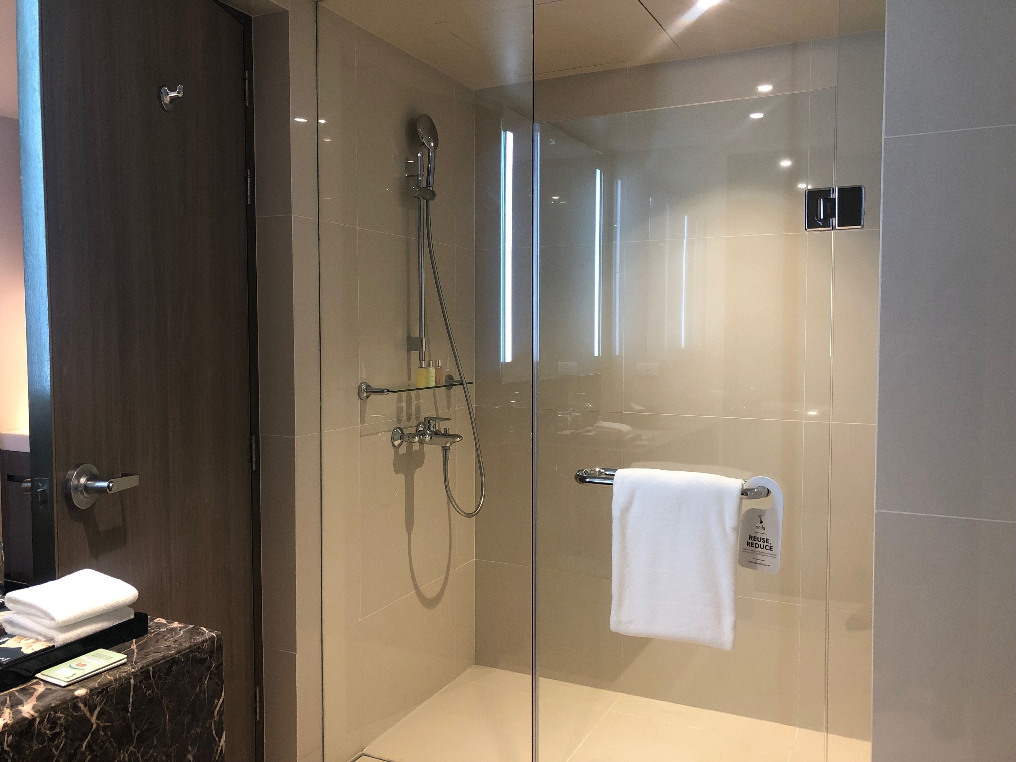 A modern shower with a glass door, a towel rack, and a hand soap dispenser.