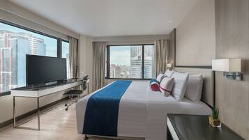 A modern hotel room with a large bed, a flat-screen TV, a desk, and a view of the cityscape.