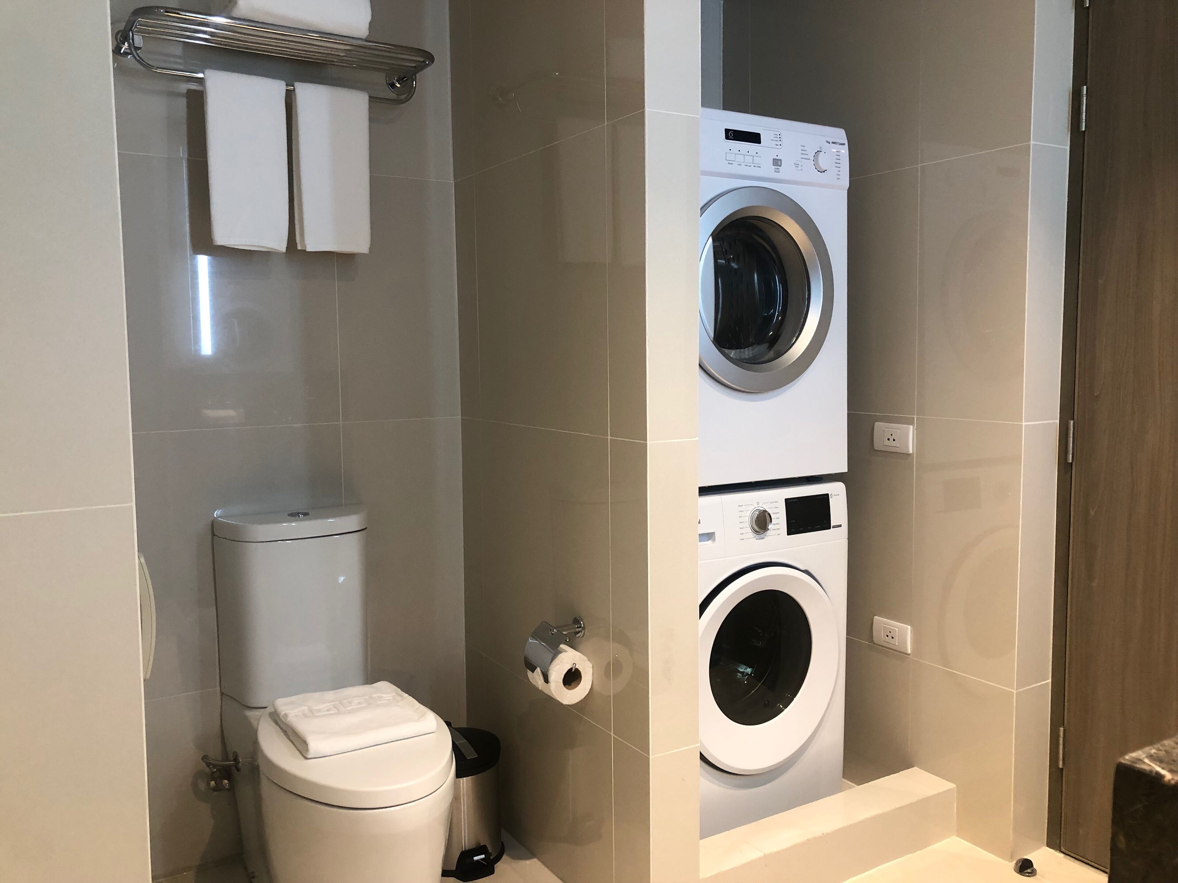 A compact bathroom with a toilet, a washing machine, and a trash bin.