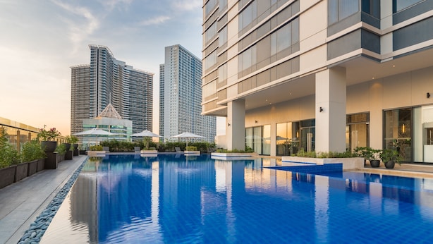 A modern hotel with a large indoor swimming pool, surrounded by high-rise buildings and outdoor seating areas. - Seda Residences Makati (Makati)
