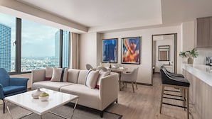 A modern living room with a sofa, coffee table, and dining area, a kitchen with bar stools, and large windows with a city view. - Seda Residences Makati (Makati)