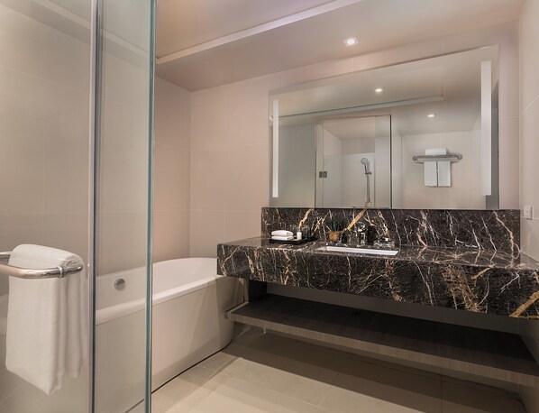 A modern bathroom with a glass-enclosed shower, a white bathtub, and a marble vanity with a sink and mirror. - Seda Residences Makati (Makati)