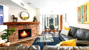A modern living room with a brick fireplace, leather sofa, and a dining area with a glass table. - Best True Ski in Out Rare slopeside @ 5 lifts Pool/Spa/Gym/WD/Parking Near Main! (Park City)
