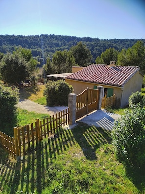 Una casa rústica con techo de tejas, rodeada por una valla de madera y abundante vegetación.