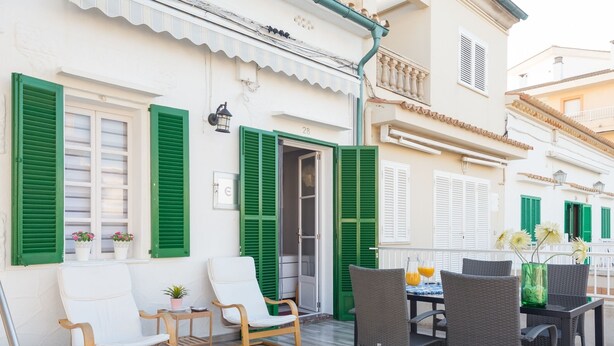 Una terraza con mobiliario exterior, una mesa y sillas, y vista a un edificio con persianas verdes.