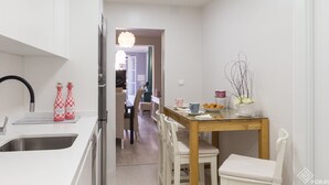 Una cocina moderna con armarios blancos, un lavamanos de acero inoxidable y un comedor con mesa de madera y sillas blancas.