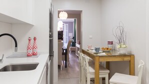 A modern kitchen with white cabinetry, a stainless steel sink, and a dining area with a wooden table and white chairs.