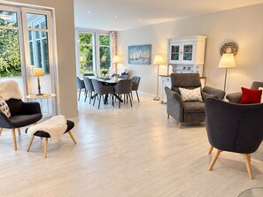 Ein modernes Wohnzimmer mit Essbereich, ausgestattet mit einer Couch, Sesseln, einem Couchtisch und einem Esstisch mit Stühlen.