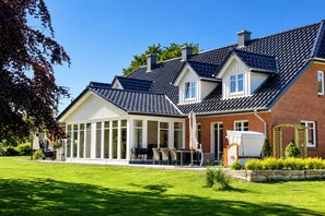 A two-story house with a covered patio, a brick exterior, and a well-maintained lawn.