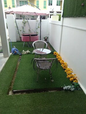 A small patio area with artificial grass, two wicker chairs, a small table, and a red and white striped umbrella. - Co. Living Suite (Bandar Seri Begawan)