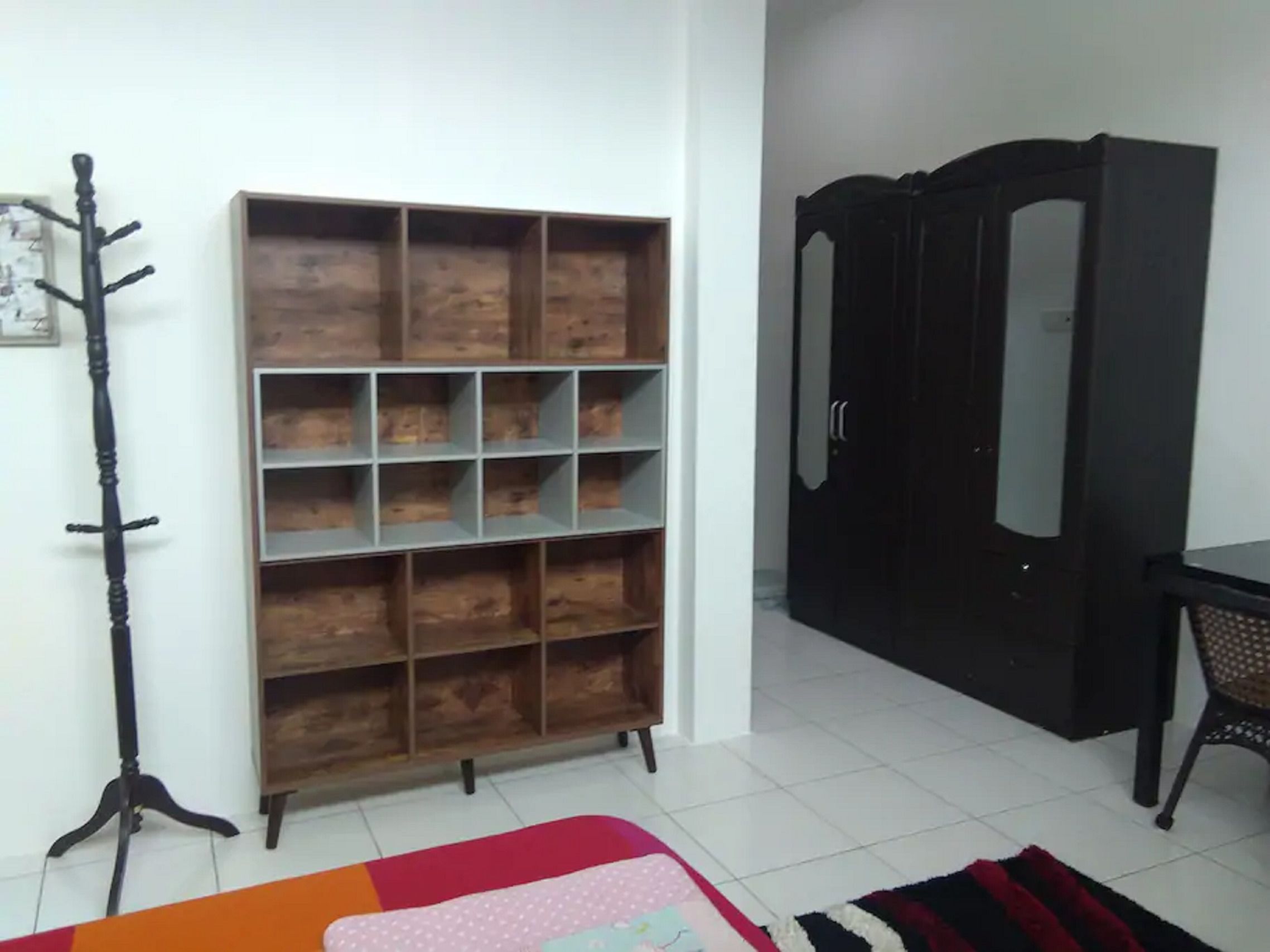 Una habitación con estantería de madera, perchero, armario y alfombra estampada.