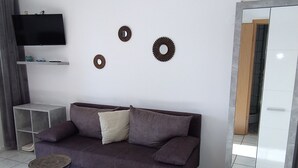 A modern living room with a dark brown sofa, two round woven stools, a flat-screen TV on the wall, and decorative wall art. - Studio apartment in Rovinj with Seaview, Terrace, Air condition, WIFI (4686-6) (Rovinj)