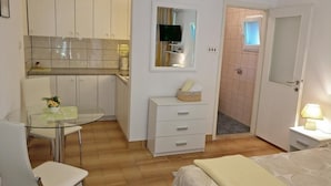 A compact room with a bed, a small table with chairs, a kitchenette with cabinets, a mirror, and a door leading to another room. - Studio apartment in Rovinj with Terrace, Air condition, WIFI, Washing machine (4686-4) (Rovinj)