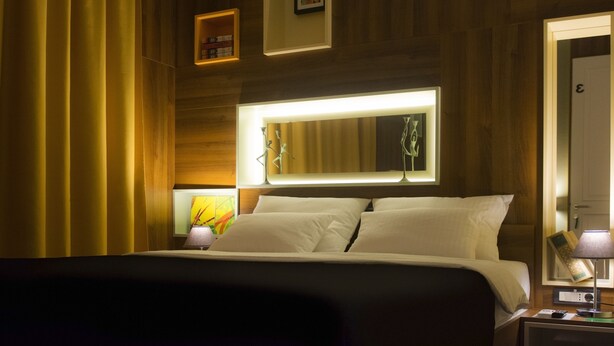 Ein Hotelzimmer mit einem großen Bett, einem Nachttisch mit Lampe, einem Spiegel und Holzvertäfelung an den Wänden.