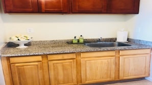 Cocina con armarios de madera, encimera de granito, un fregadero y un escurreplatos con vajilla.