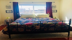 Una cama con colcha floral, una ventana con cortinas y cuadros en la pared.