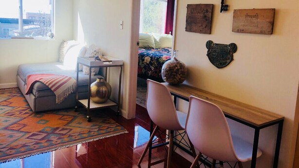 Una habitación acogedora con sofá, una pequeña mesa con sillas, una alfombra y una cama con colcha estampada.