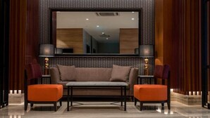 A modern lobby with a sofa and ottomans, a large mirror, and two lamps. - MPALACE HOTEL KUALA LUMPUR (Kuala Lumpur)