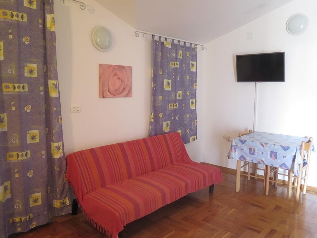 A living room with a red sofa, a table with a patterned tablecloth, and a TV mounted on the wall.