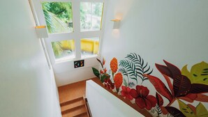 A staircase with a floral mural, a window with a view of greenery, and a wall-mounted light fixture. - Casa Tres Pochotes - Beach Front Paradise (CR)