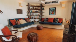 A living room with a sectional sofa, a wooden chair, a small round ottoman, a bookshelf, and a fireplace. - Casa Tres Pochotes - Beach Front Paradise (CR)