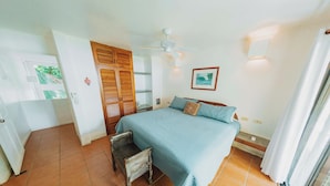A bedroom with a bed, a wooden wardrobe, a ceiling fan, and a small table. - Casa Tres Pochotes - Beach Front Paradise (CR)