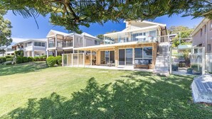 A two-story house with a covered patio, a lawn, and a large tree providing shade. - Sandy Beach House Corlette, 1/146 Sandy Point Road - Waterfront, WIFI, Aircon (Corlette)