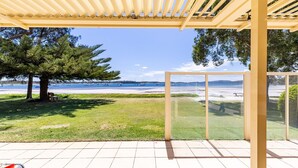 A covered outdoor area with a view of the beach and boats. - Sandy Beach House Corlette, 1/146 Sandy Point Road - Waterfront, WIFI, Aircon (Corlette)