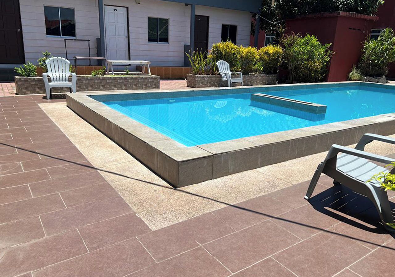 Piscina rectangular con solárium empedrado, rodeada de sillas y un banco blancos.