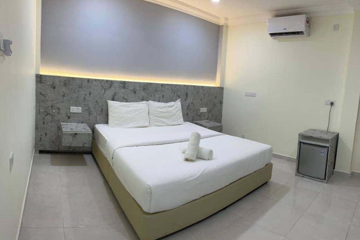 A modern bedroom with a large bed, a nightstand, a small cabinet, and an air conditioning unit.