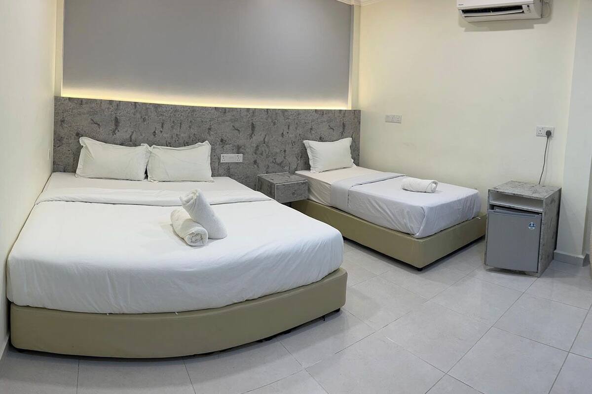 A hotel room with two beds, a small bedside table, a nightstand, and a wall-mounted air conditioner.
