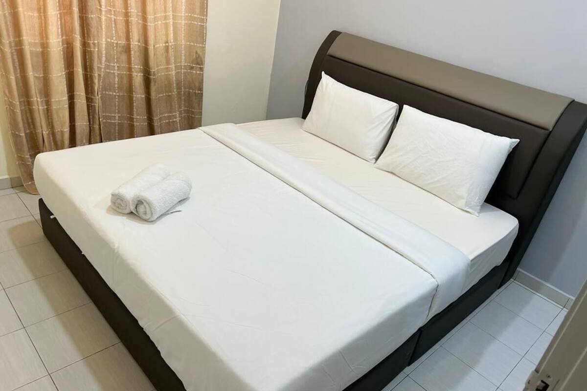 A neatly made bed with white linens and pillows, a brown headboard, and a brown curtain partially visible.